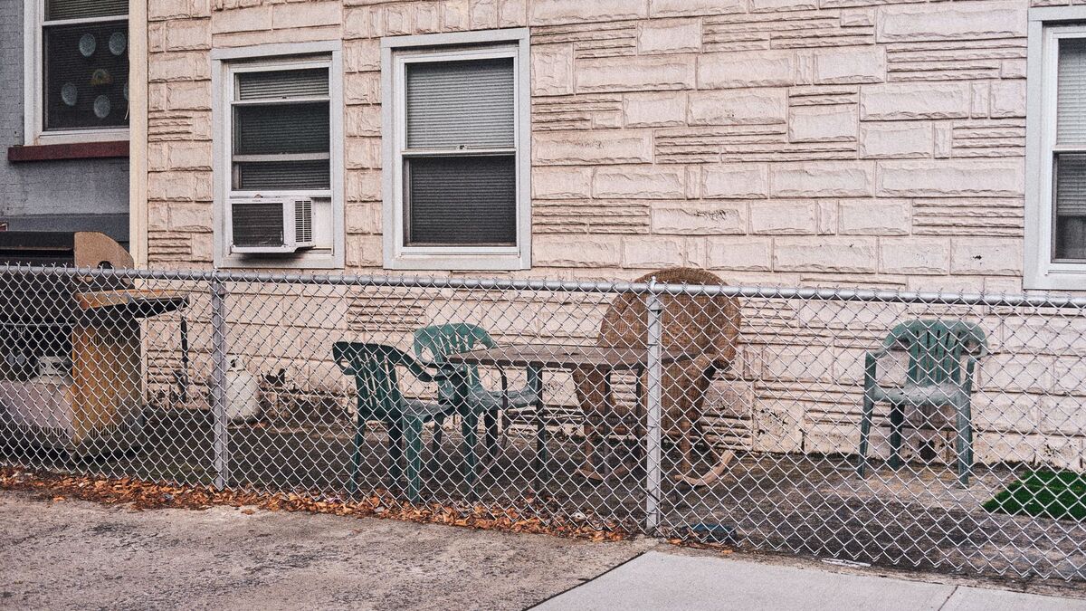 A galvanized chain link fence around a small concrete patio with chairs behind a stone-faced house