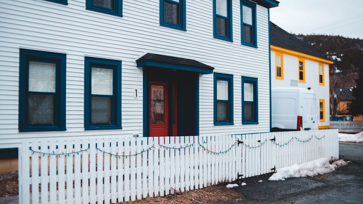 A white picket fence along the front of a two-story clapboard house on a snowy street